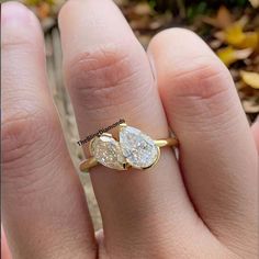 a person's hand with a gold ring and two pear shaped diamonds on it