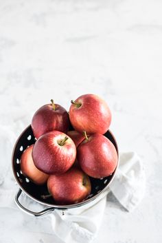 a black bowl filled with red apples on top of a white tablecloth and napkin