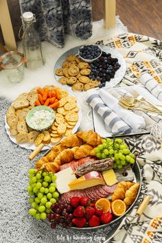 an assortment of cheeses, fruit and crackers on a platter with silverware