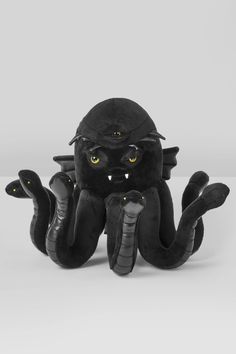 an octopus stuffed animal with yellow eyes and black skin, sitting in front of a gray background