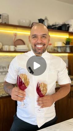 a man is holding two wine glasses in his hands and smiling at the camera while standing next to a counter