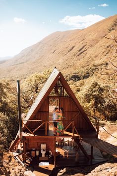 two people standing in the doorway of a small wooden cabin on top of a mountain