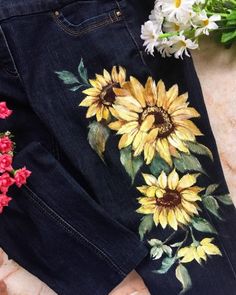 a pair of jeans with sunflowers painted on them and some flowers laying next to it