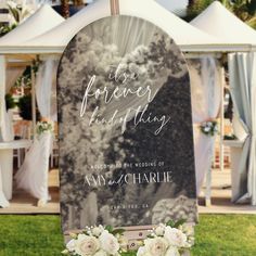 a wedding sign with flowers on it in front of a tented area for an outdoor ceremony