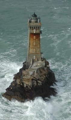 a light house sitting on top of a rock next to the ocean with waves crashing around it