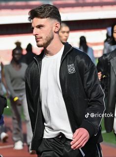 a man in black jacket and white t - shirt standing on a field with other people