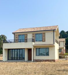 a two story house in the middle of a dry grass field with trees in the background