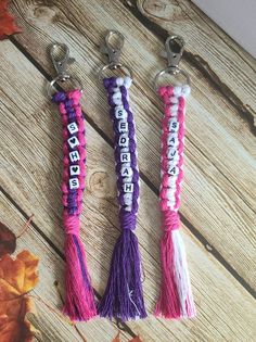 three tasseled keychains with the word happiness written in white, purple and pink