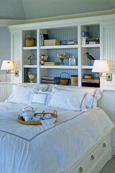 a bed with white linens and pillows in a bedroom next to a book shelf