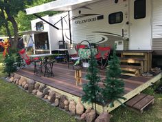 a camper is parked on the deck with chairs and trees in front of it