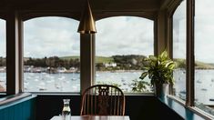 a table and chairs in a room with large windows looking out at boats on the water