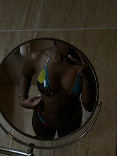 a woman in a bathing suit is looking at her cell phone while standing in front of a mirror