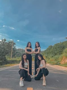 three women kneeling down in the middle of an empty road with their hands on each other's hips