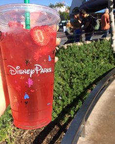 a person holding up a drink with strawberries on the top and disney park logo