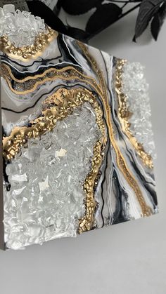 an abstract painting with gold and silver accents on a white table top next to a plant