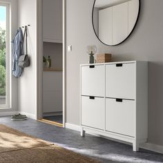 a white cabinet sitting in front of a window next to a mirror and coat rack