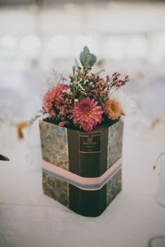 a vase with flowers in it sitting on a white table cloth covered tablecloth at a wedding reception