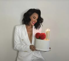 a woman holding a cake with candles on it in front of her face and wearing a white suit