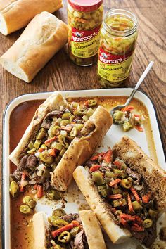 two sandwiches on a plate with pickles and mustard next to some bread roll rolls