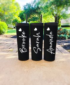 three black tumblers with white writing on them sitting in the middle of a sidewalk