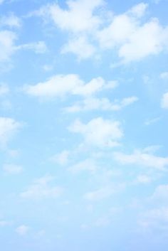 two people standing on the beach flying a kite in the blue sky with white clouds