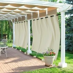 a patio covered in white curtains next to a picnic table and chairs with potted plants