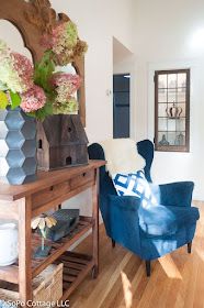 a blue chair sitting next to a wooden table with flowers on it and a mirror