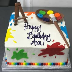 a birthday cake decorated with an easel, paintbrush and acrylic colors