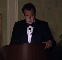 a man in a tuxedo standing at a podium with his hands behind him