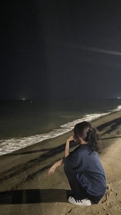 a woman is sitting on the beach at night