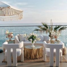 an outdoor seating area with white furniture and flowers on the table next to the ocean