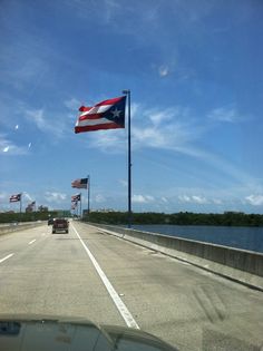 an american flag is flying over the water from a highway with cars driving on it