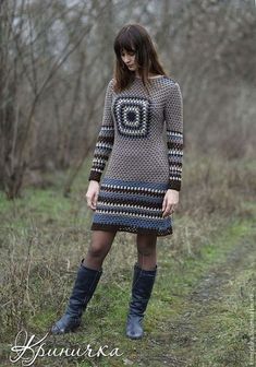 a woman is standing in the grass wearing boots and a sweater dress with an ornament on it