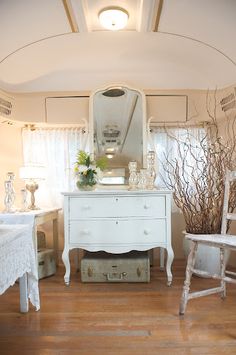 a white dresser sitting next to a mirror on top of a wooden floor covered in furniture