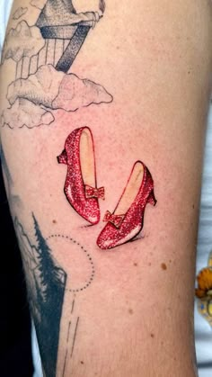 a woman's arm with a red pair of ballet shoes on it and an airplane in the sky