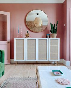 a living room with pink walls and white furniture in the corner, along with a round mirror on the wall