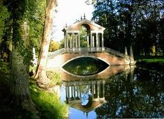 an old bridge over a pond in the middle of a park with trees around it