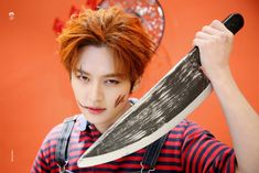 a young man with red hair holding a large knife in front of an orange wall