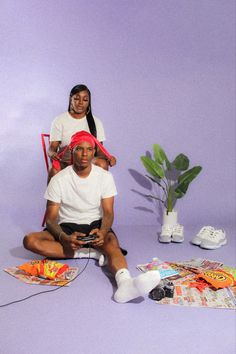 a man and woman sitting on the ground in front of a purple background, one holding a game controller