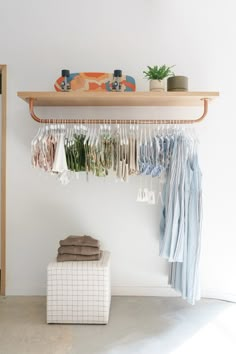 clothes hanging on a rack in front of a white wall with a wooden shelf above it