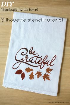 an embroidered tea towel with the words be grateful written in brown on it and leaves