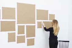 a woman is holding up some brown paper to the wall with pink tape on it