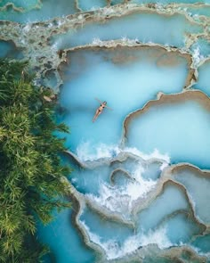 an aerial view of a man swimming in the blue lagoon, with trees surrounding it