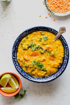 a bowl filled with yellow lentils and garnished with cilantro, carrots, corian seeds and lime