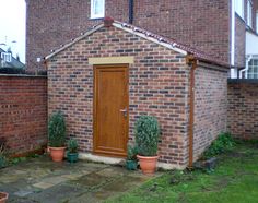 a brick building with potted plants in front of it and a wooden door on the side