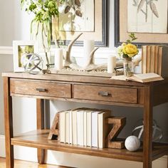 a wooden table topped with books and vases filled with flowers next to two framed pictures