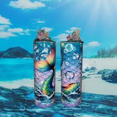 two colorful vases sitting next to each other on a beach with blue sky and clouds in the background