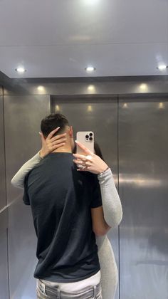 a man and woman standing in front of an elevator taking a selfie with their cell phone