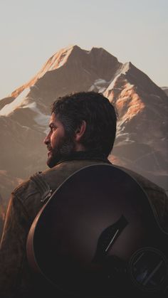 a man standing in front of a mountain with a guitar strapped to his back and looking at the sky