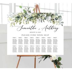 an easel with greenery and white flowers on it is the centerpiece for a seating